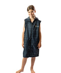 Child wearing a schmik swim parka in black. Black swim parka has removable sleeves and is zipped up.