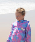 Child wearing pink mermaid print swim parka standing on the beach.
