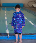 7 year old boy standing next to a pool wearing a schmik swim parka in a blue fishbone print. 