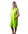 Lady is standing wearing a fluro green swim parka. Schmik fluro green swim parka is long and zipped up. Lady has her hand in the swim parkas pockets. 