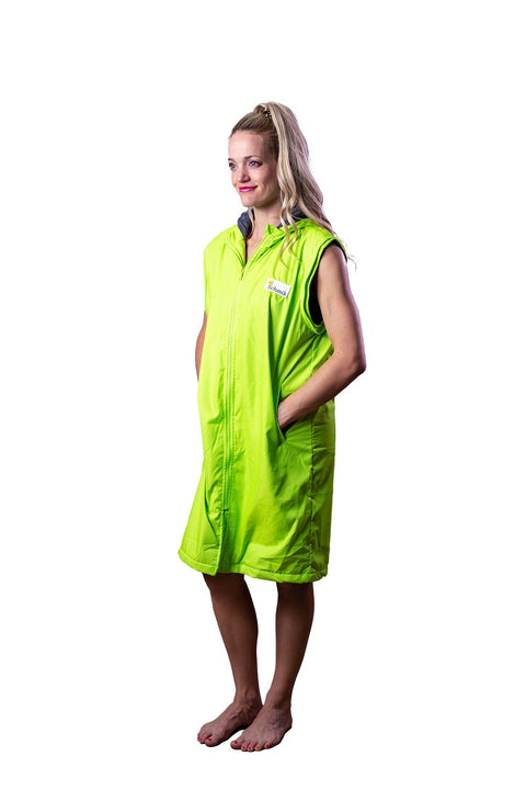 Lady is standing wearing a fluro green swim parka. Schmik fluro green swim parka is long and zipped up. Lady has her hand in the swim parkas pockets. 